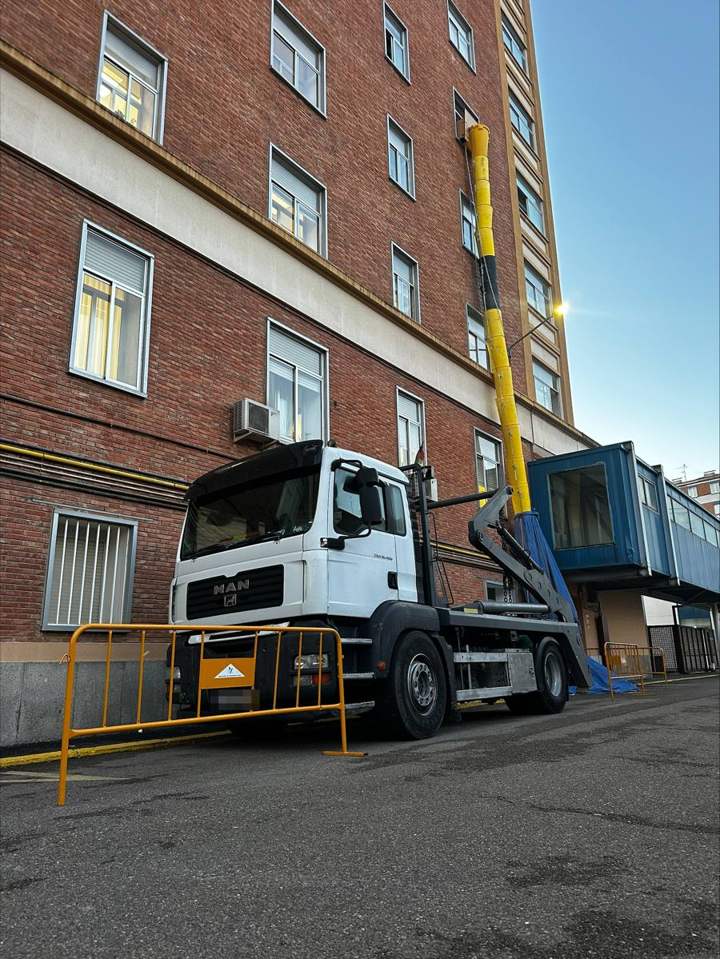 Bajante de escombros por fachada y camión portacontenedores en una obra de Madrid